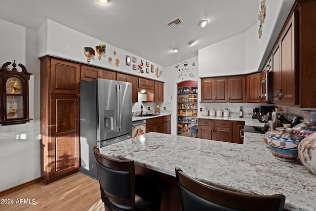 kitchen with light wood-type flooring, kitchen peninsula, a kitchen breakfast bar, stainless steel appliances, and high vaulted ceiling