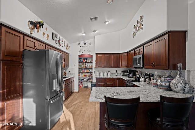 kitchen featuring a breakfast bar, light hardwood / wood-style floors, kitchen peninsula, backsplash, and appliances with stainless steel finishes