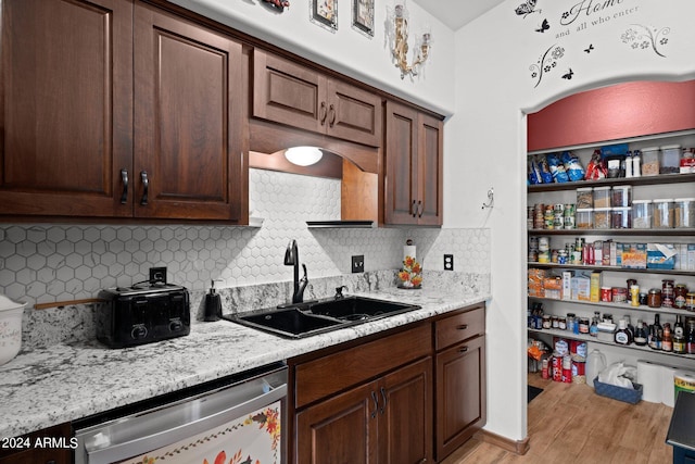 kitchen with light wood-type flooring, decorative backsplash, stainless steel dishwasher, and sink