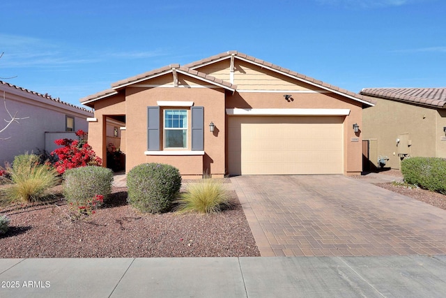 view of front of property with a tiled roof, decorative driveway, an attached garage, and stucco siding