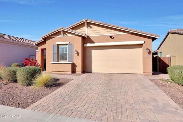 single story home with a garage, a tiled roof, fence, decorative driveway, and stucco siding