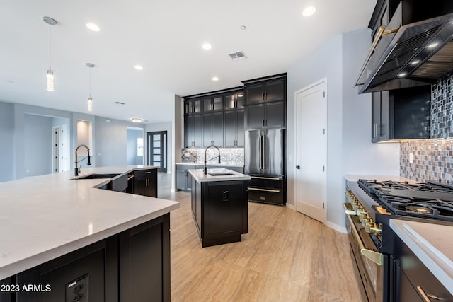 kitchen with tasteful backsplash, a kitchen island with sink, wall chimney range hood, decorative light fixtures, and high quality appliances