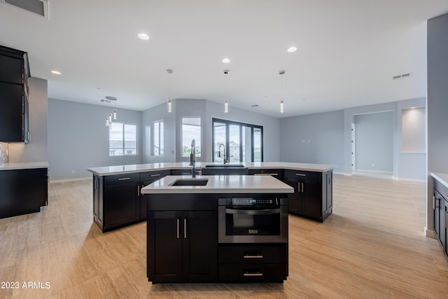 kitchen with a kitchen island with sink, oven, pendant lighting, and light hardwood / wood-style floors