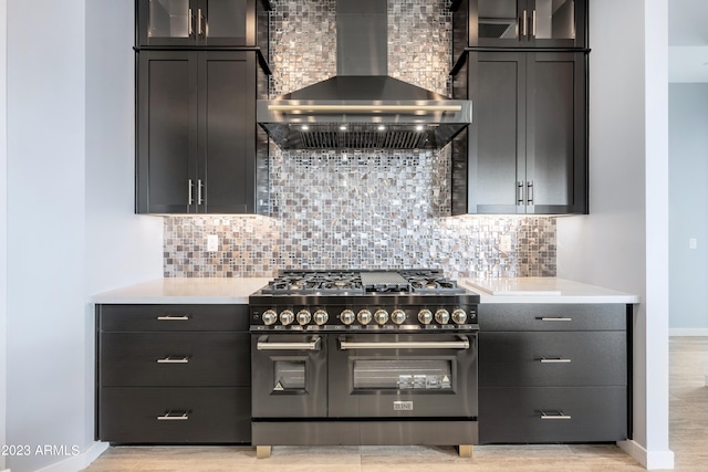 kitchen with decorative backsplash, light hardwood / wood-style flooring, range with two ovens, and wall chimney exhaust hood