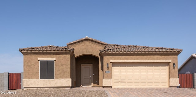 mediterranean / spanish-style home featuring a garage, a tile roof, decorative driveway, and stucco siding