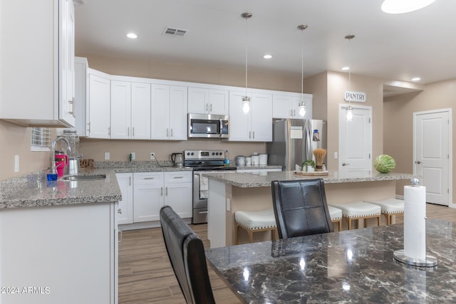 kitchen with hanging light fixtures, appliances with stainless steel finishes, white cabinets, and a center island