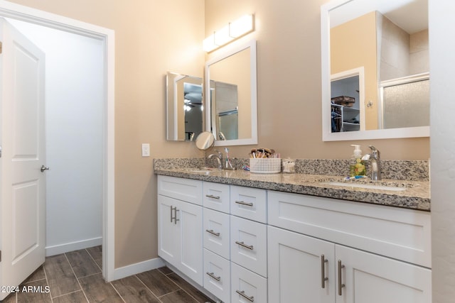 bathroom featuring double vanity, baseboards, a sink, and wood finish floors