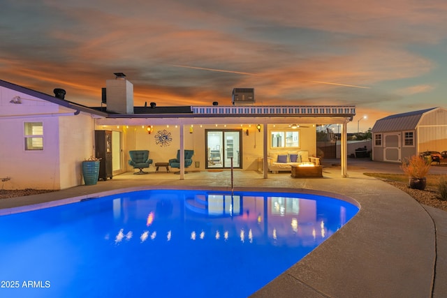 pool at dusk featuring a storage unit, a patio area, and a fire pit