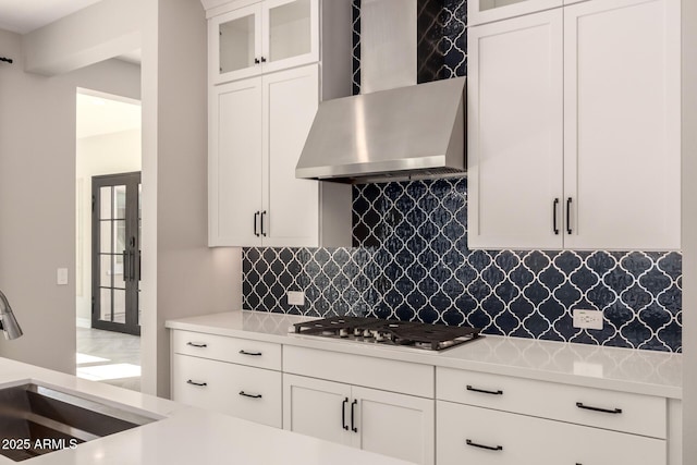 kitchen with stainless steel gas cooktop, light countertops, backsplash, a sink, and wall chimney exhaust hood