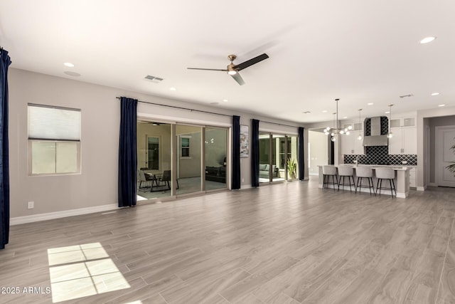 living area featuring light wood-style flooring, visible vents, ceiling fan with notable chandelier, and plenty of natural light