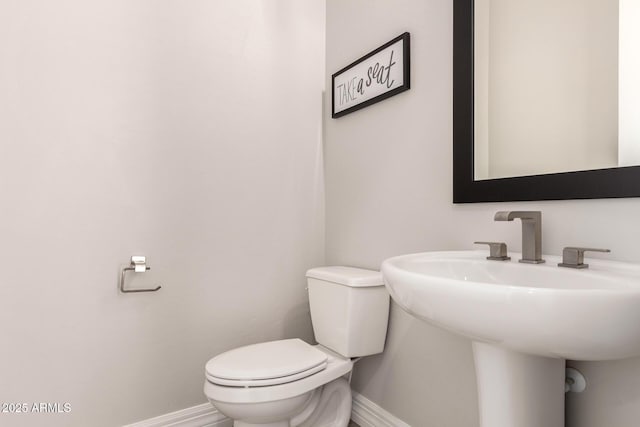 half bathroom featuring baseboards, toilet, and a sink