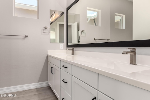 full bathroom with double vanity, wood finished floors, baseboards, and a sink