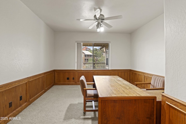 office with a wainscoted wall, ceiling fan, light carpet, and wooden walls