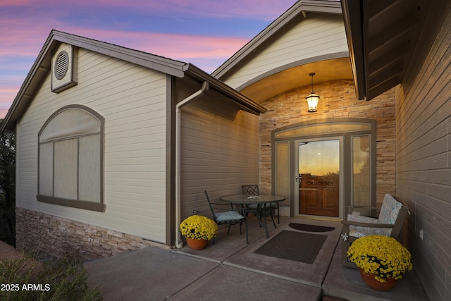 exterior entry at dusk featuring stone siding and a patio