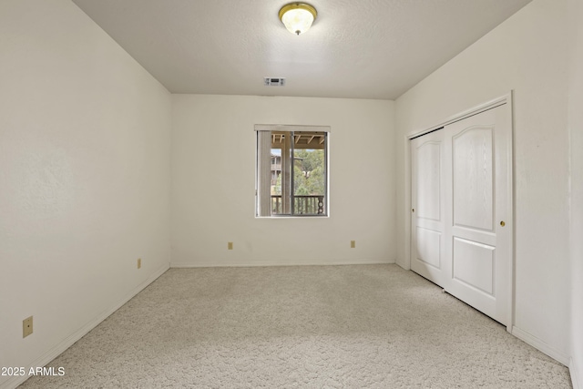 unfurnished bedroom with a textured ceiling, carpet floors, visible vents, baseboards, and a closet