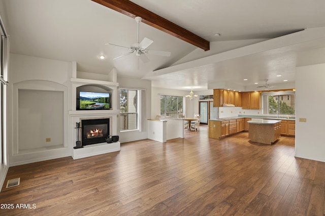 unfurnished living room featuring vaulted ceiling with beams, wood-type flooring, visible vents, a glass covered fireplace, and ceiling fan with notable chandelier