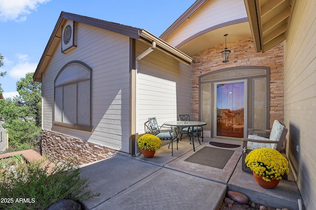 view of exterior entry with stone siding, a patio area, and outdoor dining area