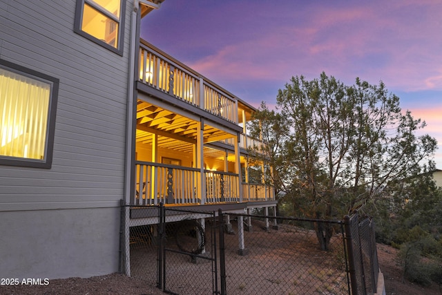 property exterior at dusk with a deck, a gate, fence, and a balcony