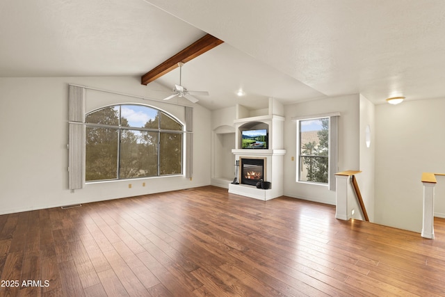 unfurnished living room featuring vaulted ceiling with beams, hardwood / wood-style floors, a glass covered fireplace, and visible vents