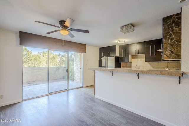 kitchen featuring hardwood / wood-style flooring, ceiling fan, a kitchen bar, stainless steel fridge with ice dispenser, and kitchen peninsula