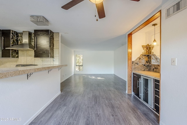 kitchen with decorative light fixtures, dark hardwood / wood-style floors, wall chimney range hood, beverage cooler, and backsplash