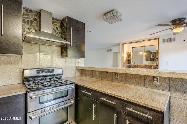 kitchen with tasteful backsplash, dark brown cabinetry, wall chimney exhaust hood, and range with two ovens