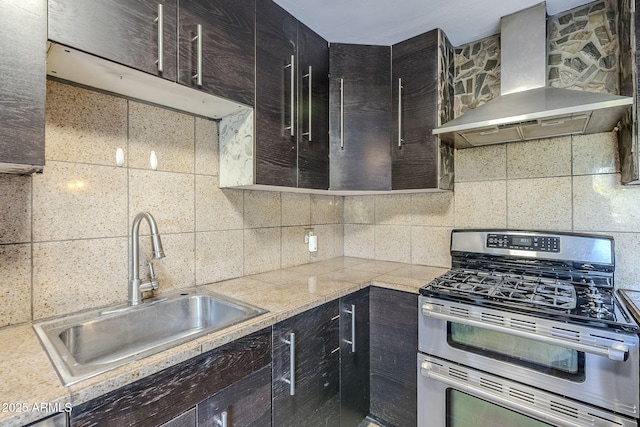 kitchen with double oven range, sink, wall chimney range hood, and backsplash