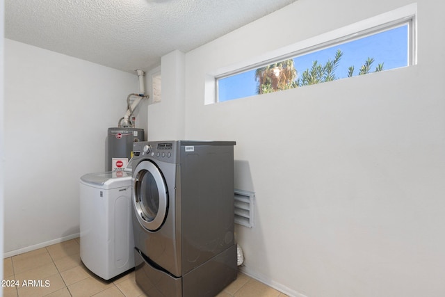 laundry area featuring washer and dryer, light tile patterned flooring, a textured ceiling, and water heater