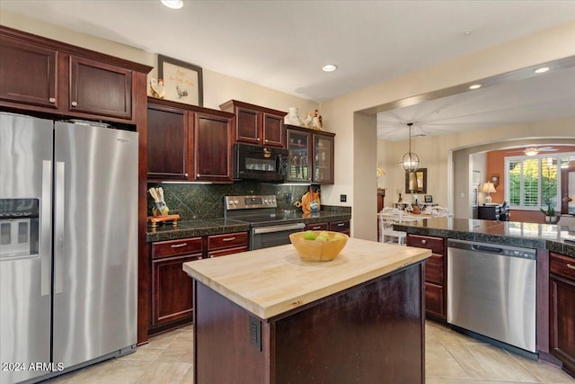 kitchen with appliances with stainless steel finishes, backsplash, a kitchen island, butcher block counters, and light tile patterned flooring