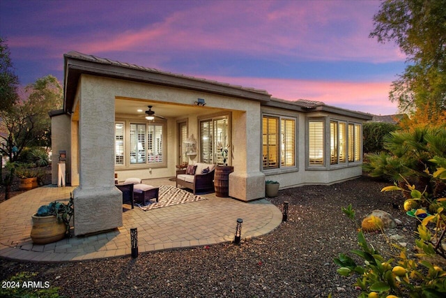 back house at dusk with ceiling fan, an outdoor hangout area, and a patio