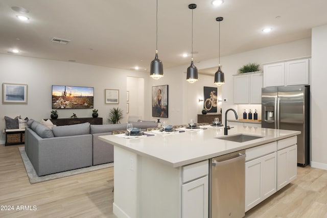 kitchen with light wood-type flooring, a sink, open floor plan, appliances with stainless steel finishes, and white cabinets