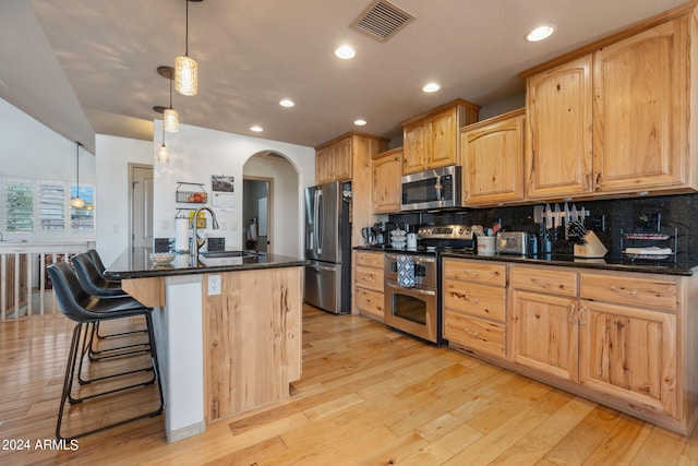 kitchen featuring a kitchen island with sink, decorative light fixtures, stainless steel appliances, and light hardwood / wood-style floors