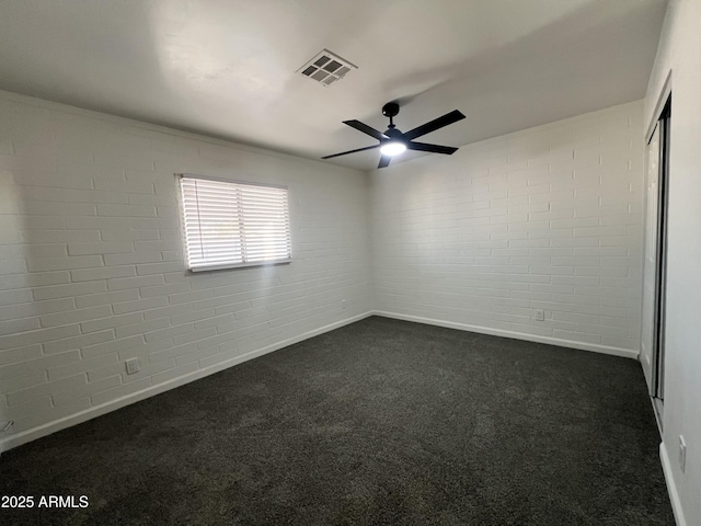 spare room with dark colored carpet, ceiling fan, and brick wall