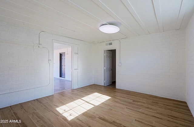 empty room with brick wall and hardwood / wood-style floors