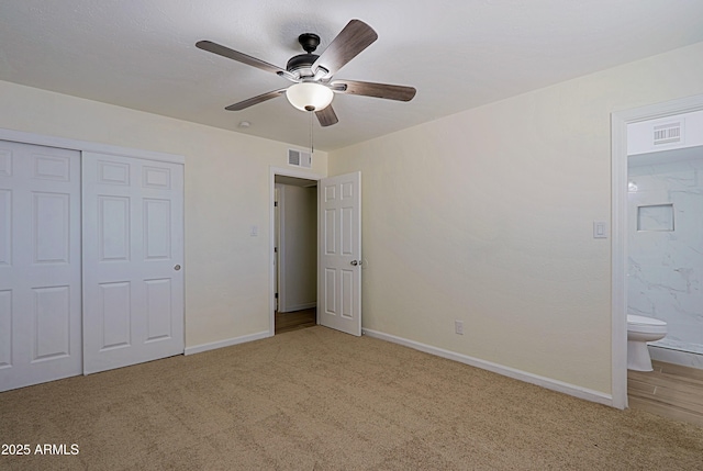 unfurnished bedroom with ceiling fan, light carpet, a closet, and ensuite bath