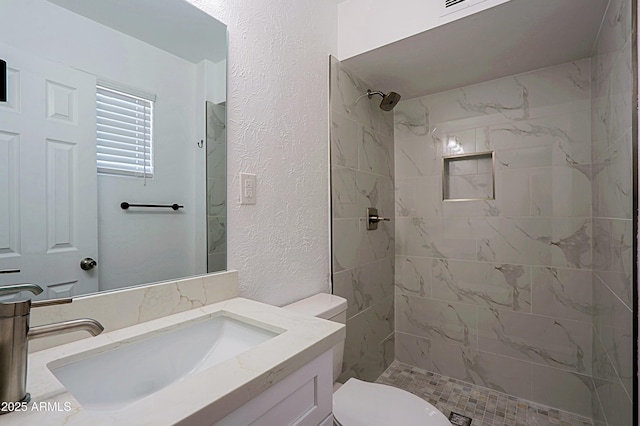 bathroom with toilet, vanity, and a tile shower