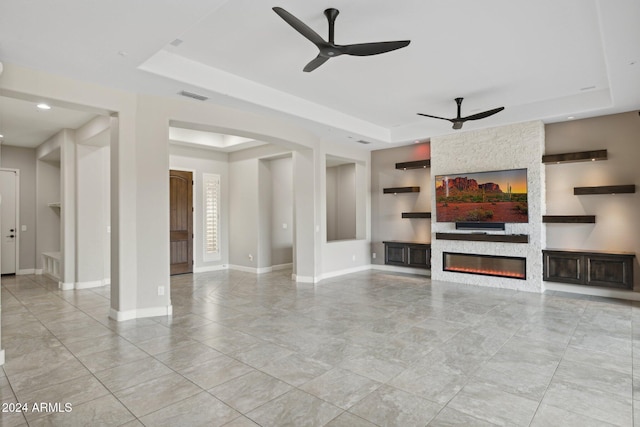 unfurnished living room with a raised ceiling, ceiling fan, and a fireplace