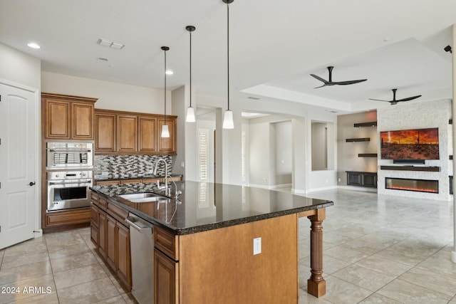 kitchen with appliances with stainless steel finishes, a raised ceiling, sink, a center island with sink, and decorative light fixtures