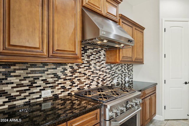 kitchen with stainless steel stove, ventilation hood, backsplash, dark stone counters, and light tile patterned flooring