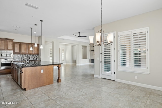 kitchen with pendant lighting, a kitchen island with sink, dark stone counters, ceiling fan with notable chandelier, and appliances with stainless steel finishes