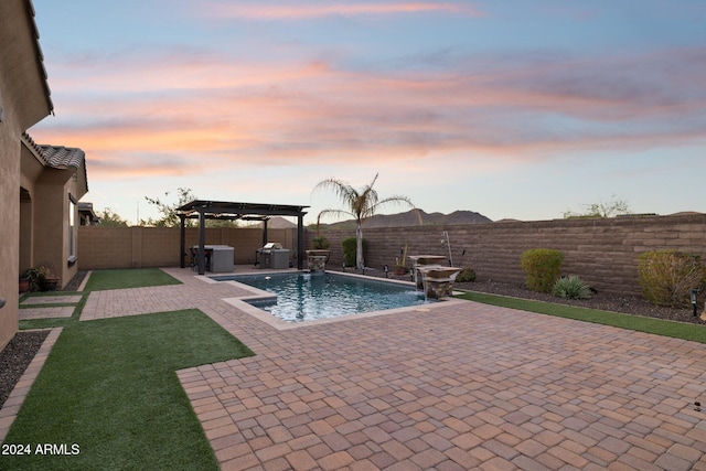 pool at dusk featuring pool water feature, a pergola, and a patio