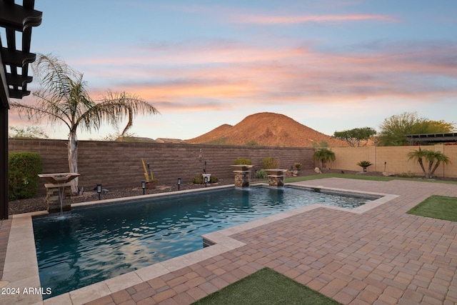 pool at dusk with pool water feature and a mountain view