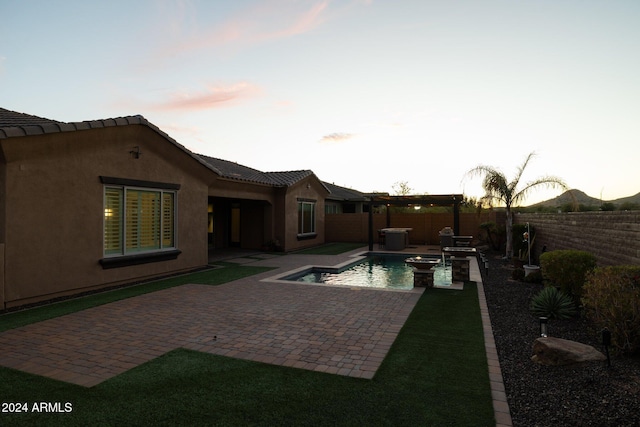 pool at dusk featuring a patio area and a jacuzzi