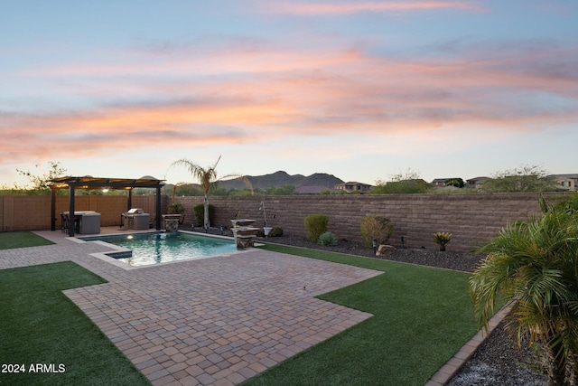 pool at dusk featuring a pergola, a patio, pool water feature, a mountain view, and a yard