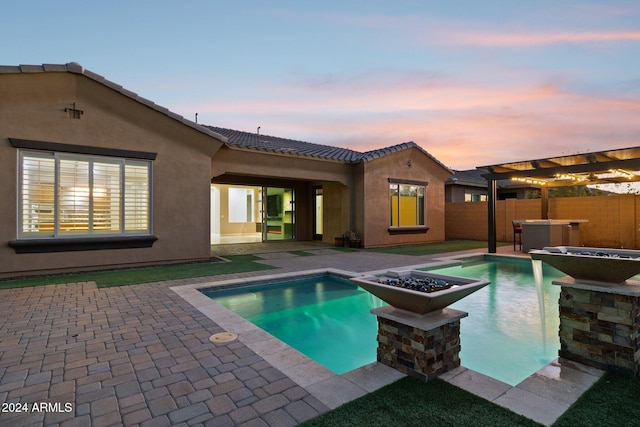 pool at dusk featuring a patio area and a jacuzzi