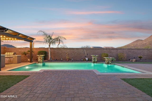 pool at dusk with area for grilling, pool water feature, and a patio