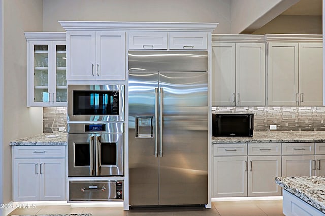 kitchen featuring white cabinets, built in appliances, and tasteful backsplash