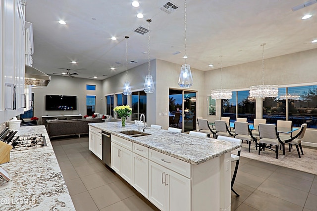 kitchen with a kitchen island with sink, ceiling fan with notable chandelier, sink, decorative light fixtures, and white cabinetry