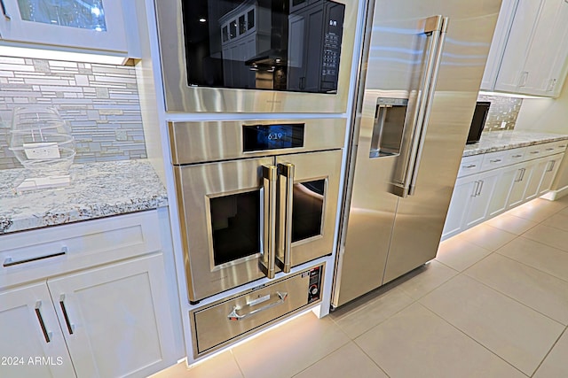 kitchen with white cabinetry, light stone countertops, decorative backsplash, light tile patterned floors, and appliances with stainless steel finishes