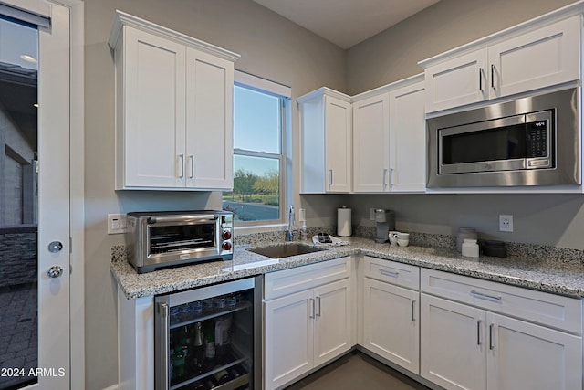 kitchen featuring stainless steel microwave, sink, wine cooler, light stone counters, and white cabinets